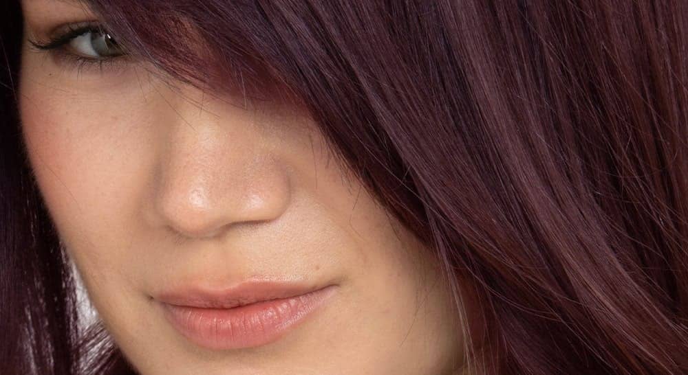 Primer plano de cabello caoba largo y brillante en el rostro de una mujer, mostrando los resultados de una coloración con ingredientes naturales