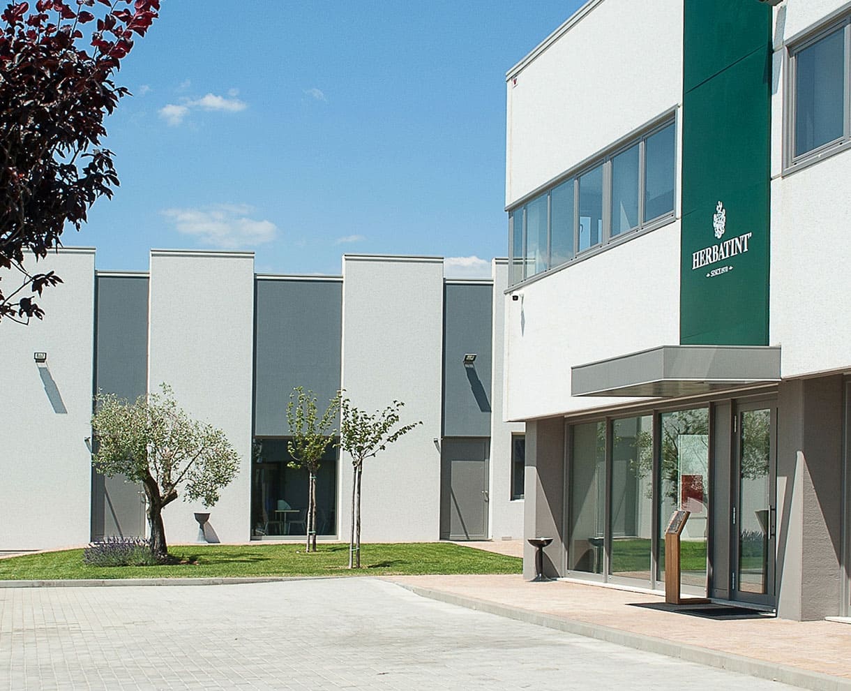 Eingang des Herbatint-Firmensitzes mit Garten, Bäumen und weiß-grünen Fassaden