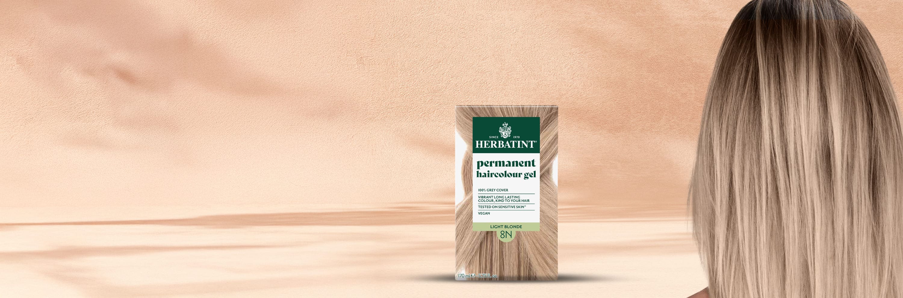 Doos van Herbatint 8N lichtblonde permanente kleurgel naast het gladde, glanzende haar van een vrouw in een natuurlijke blondtint