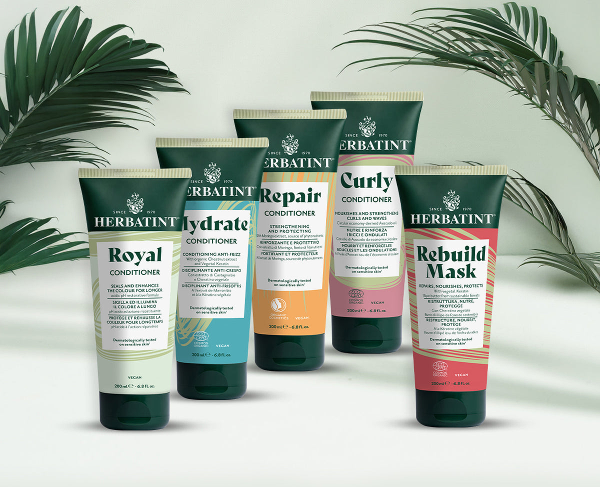Five Herbatint conditioners for treated and sensitive hair – Royal, Hydrate, Repair, Curly and Rebuild Mask variants on a light background with decorative green palm leaves