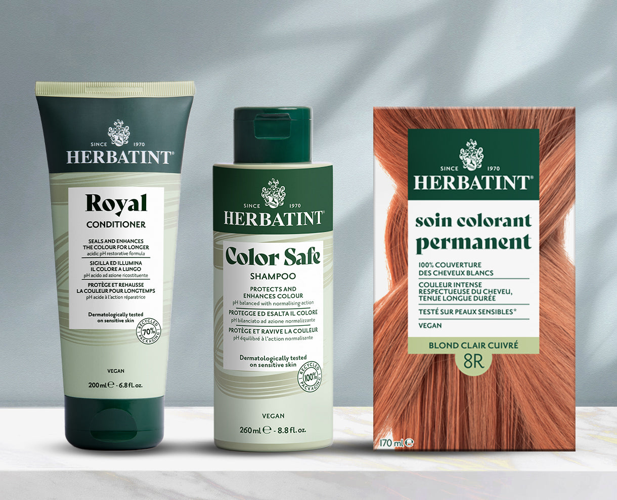 Gamme de produits Herbatint présentée sur fond gris, incluant shampooing, après-shampooing et gel colorant permanent sur une table en marbre.