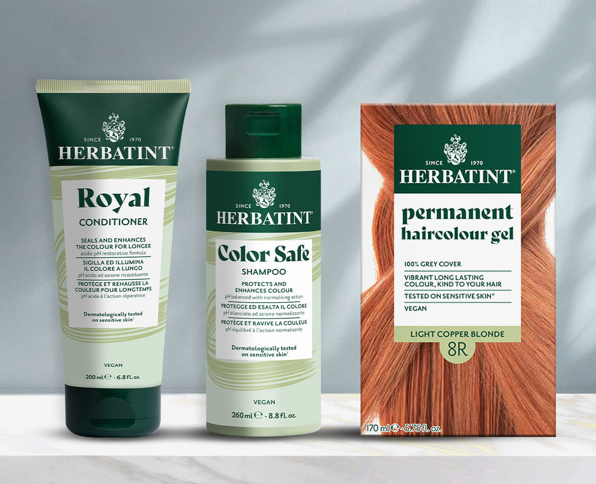 Linha de produtos Herbatint apresentada sobre fundo cinzento, incluindo champô, amaciador e gel colorante permanente sobre uma mesa de mármore.