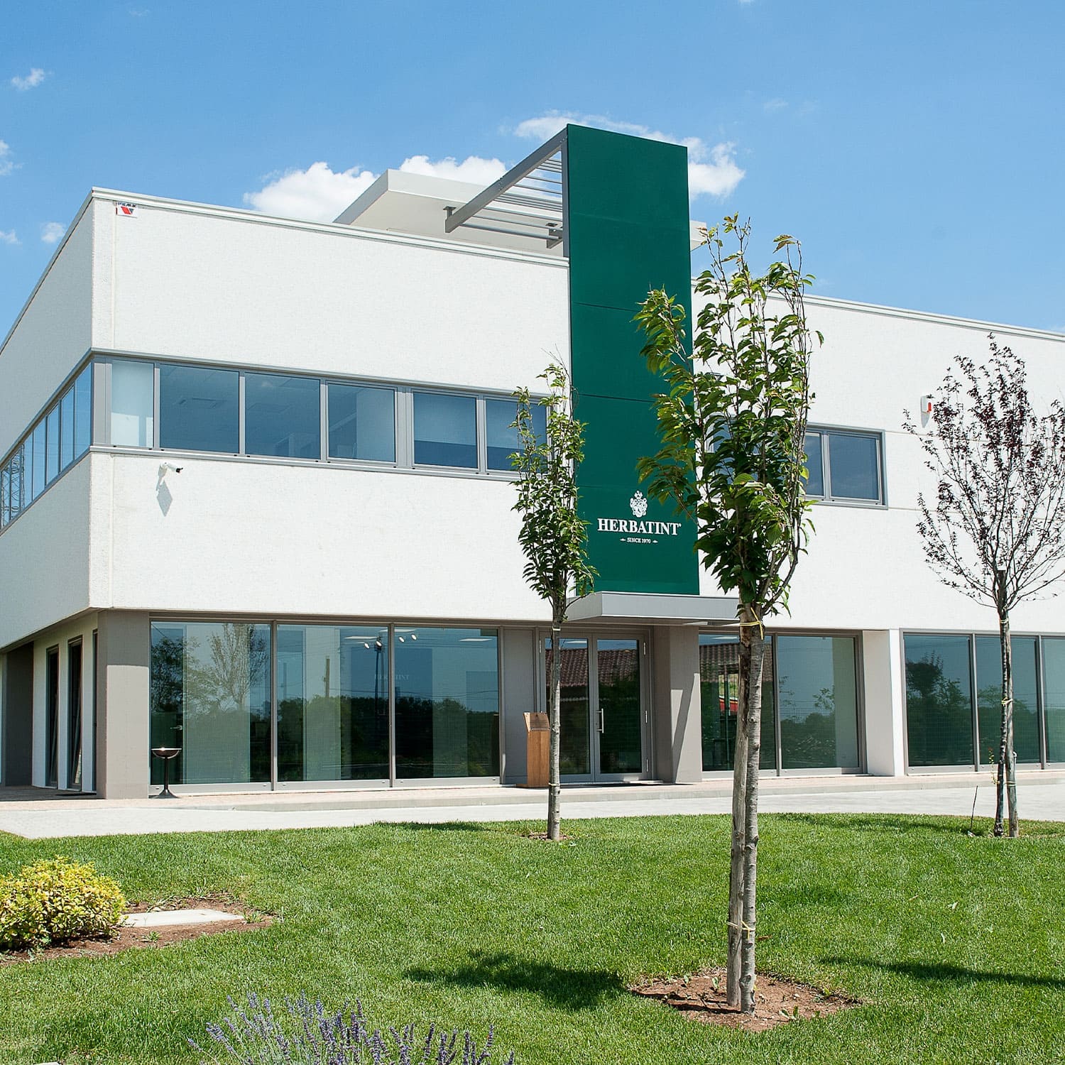 Sede Herbatint con giardino alberato e logo visibile sull'ingresso dell’edificio.