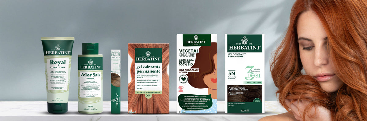 Linea completa di prodotti Herbatint esposta su fondo neutro, inclusi shampoo, balsamo, mascara per capelli, gel coloranti permanenti e vegetal color. A destra, una donna accarezza i suoi lunghi capelli ramati