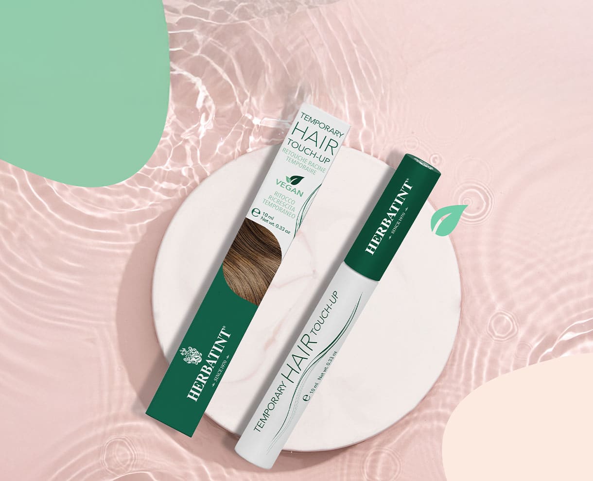 Mascara copri-ricrescita Herbatint su sfondo rosa con foglia tropicale. Prodotto vegano per ritocco temporaneo dei capelli bianchi