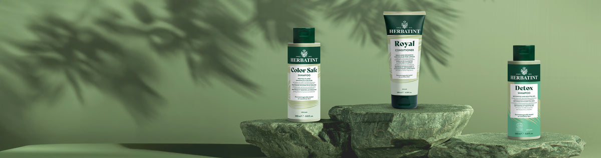 Linea hair care Herbatint con shampoo Color Safe, balsamo Royal e shampoo Detox posizionati sopra delle pietre su sfondo verde naturale