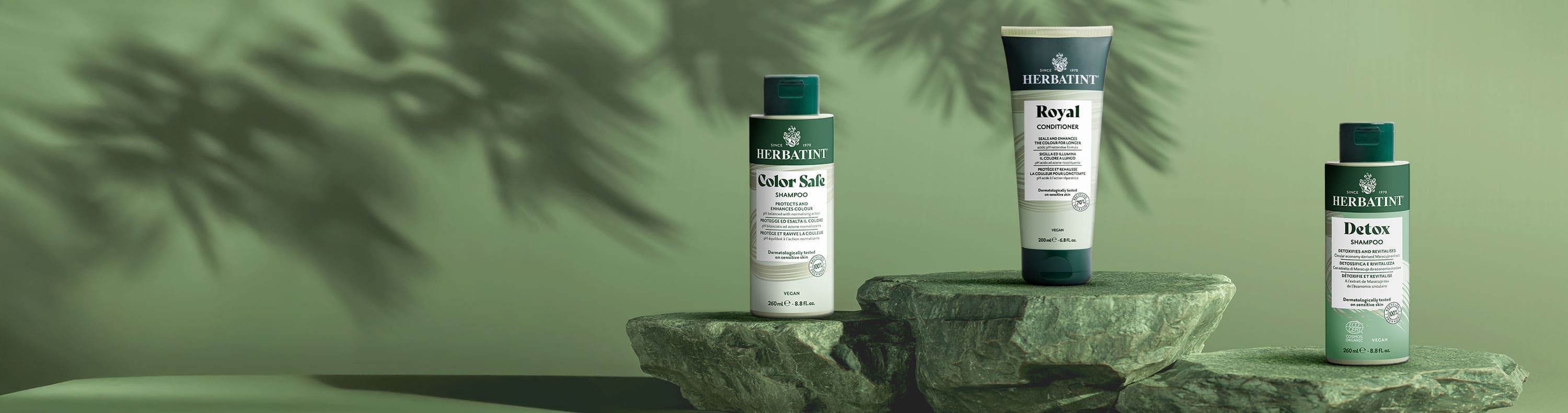 Herbatint Haarpflegelinie: Color Safe Shampoo, Royal Conditioner und Detox Shampoo auf Steinen arrangiert vor natürlichem grünem Hintergrund