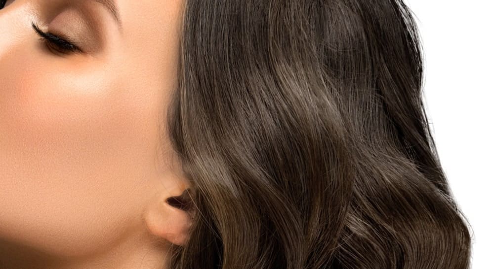 Cheveux châtain cendré ondulés avec de subtils reflets naturels, illustrant un résultat de couleur doux