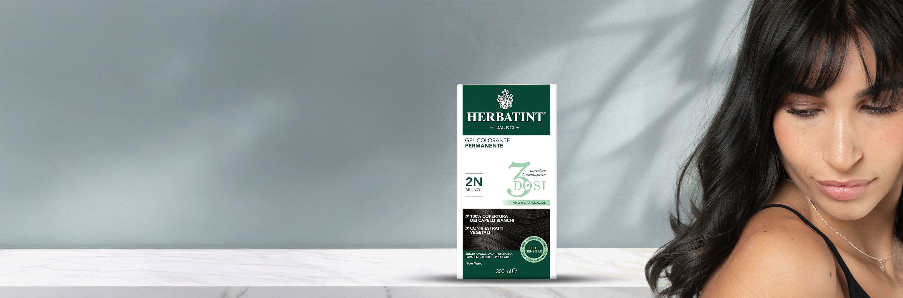 Confezione di gel colorante permanente Herbatint 2N bruno 300 ml con 3 dosi, accanto a una donna con capelli scuri lisci e luminosi