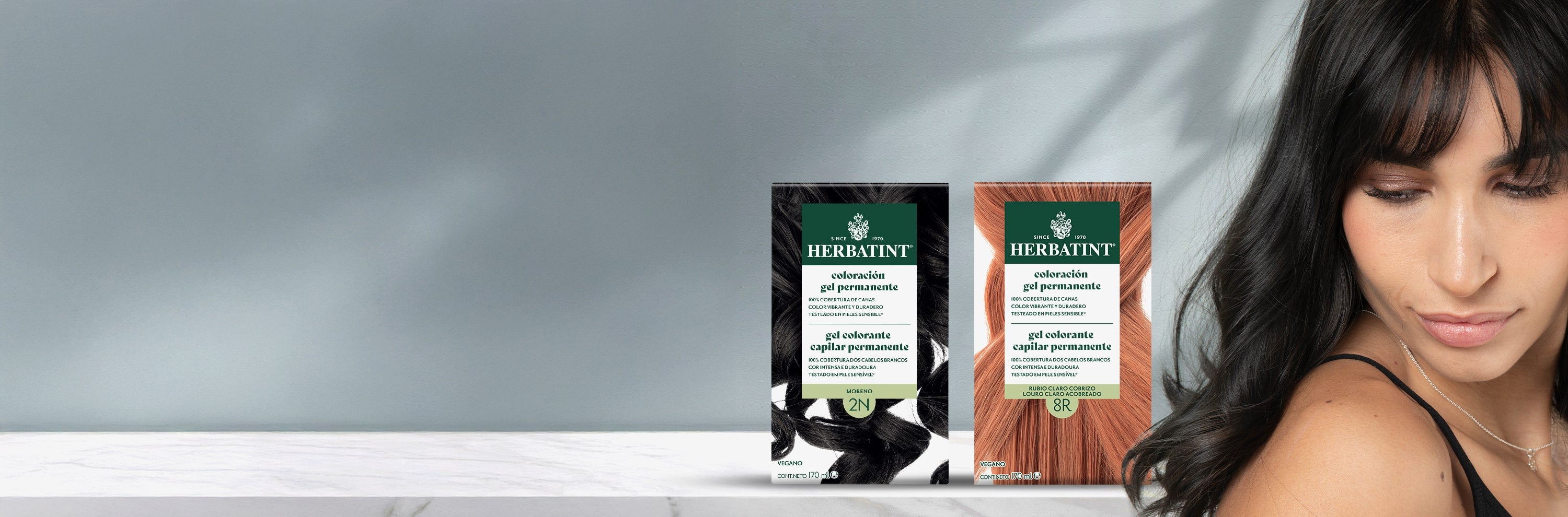 Três embalagens de coloração Herbatint em diferentes tons, 2N castanho escuro e 8R loiro claro acobreado, ao lado de uma mulher com cabelo escuro e brilhante