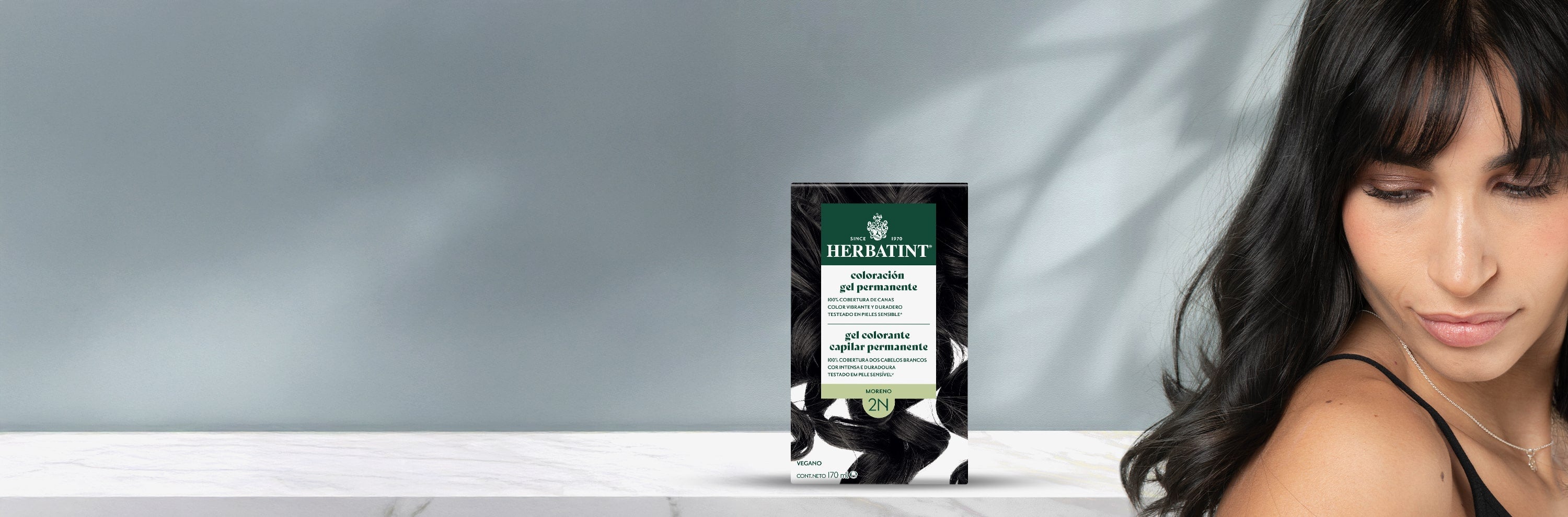 Envase del gel colorante permanente Herbatint 2N castaño junto a una mujer con el cabello oscuro, liso y brillante.
