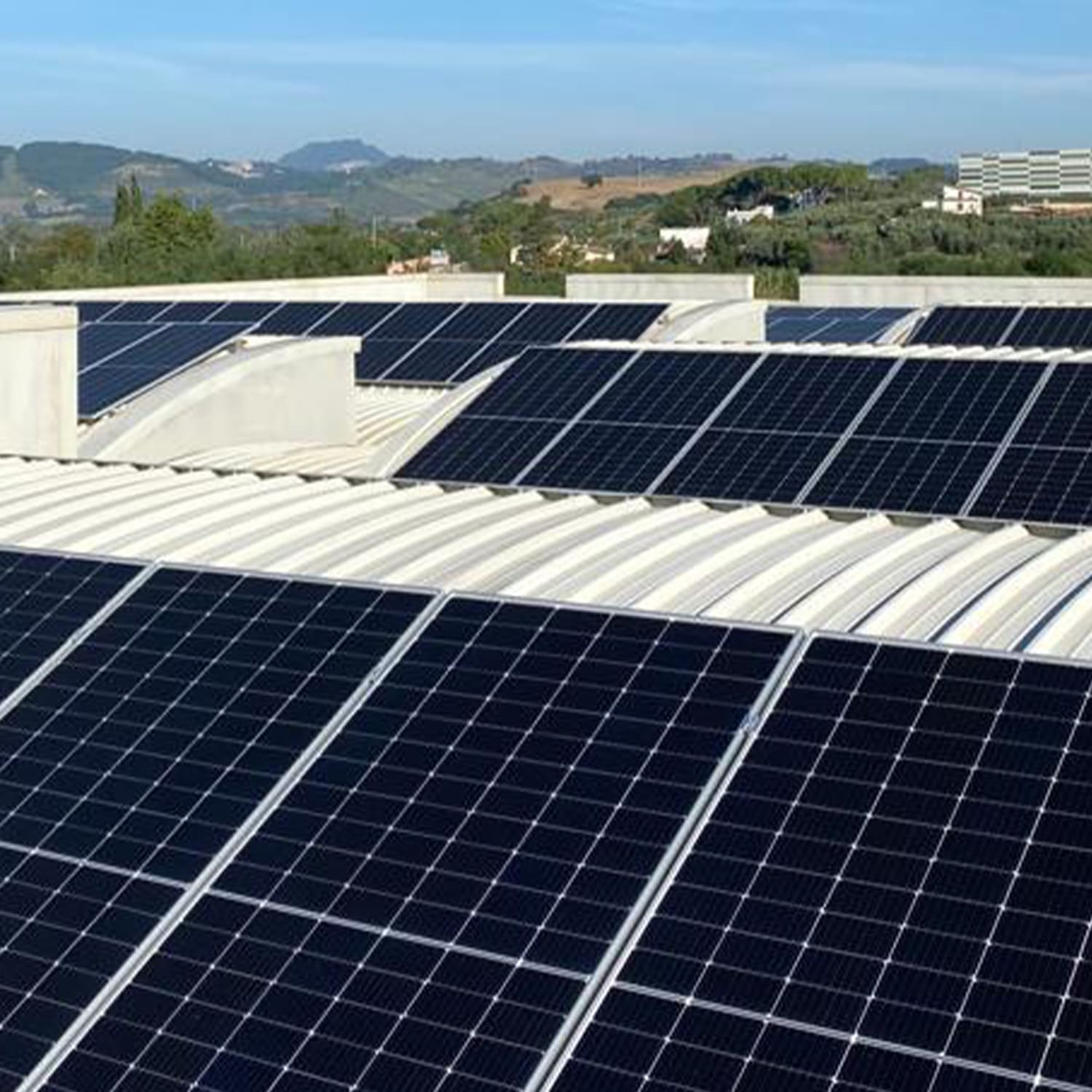 Painéis solares fotovoltaicos nos telhados dos edifícios da Herbatint em meio a uma paisagem verdejante e montanhosa, ilustrando o compromisso da empresa com a sustentabilidade energética e a autoprodução renovável
