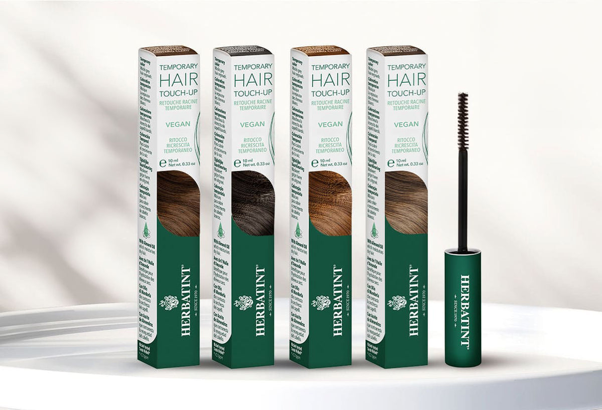 Volledige Herbatint-haarmascalijn in vier tinten met borstelapplicators en groene verpakking, gepresenteerd op een witte tafel in een zacht verlichte natuurlijke setting