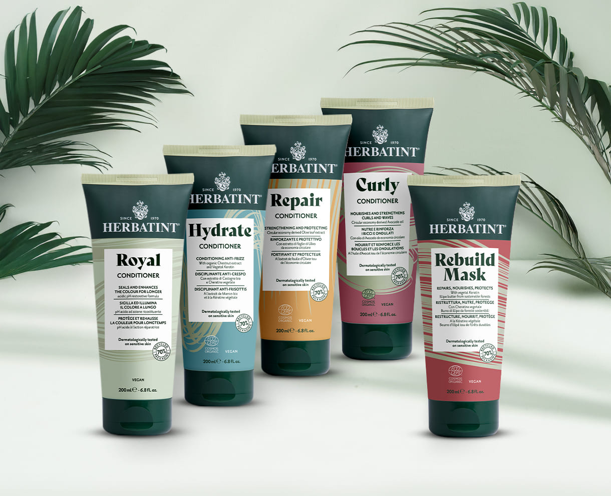 Cinq après-shampoings Herbatint pour cheveux traités et sensibles – variantes Royal, Hydrate, Repair, Curly et Rebuild Mask sur fond clair avec feuilles de palmier vertes décoratives
