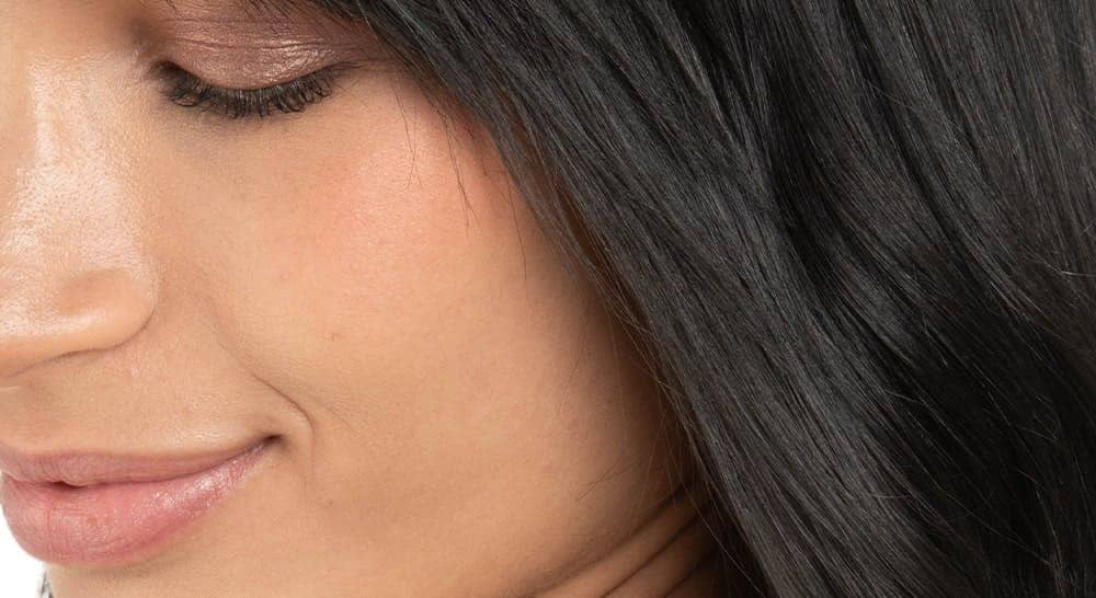 Primer plano de cabello negro natural y brillante enmarcando el rostro sonriente de una mujer, mostrando el resultado del color