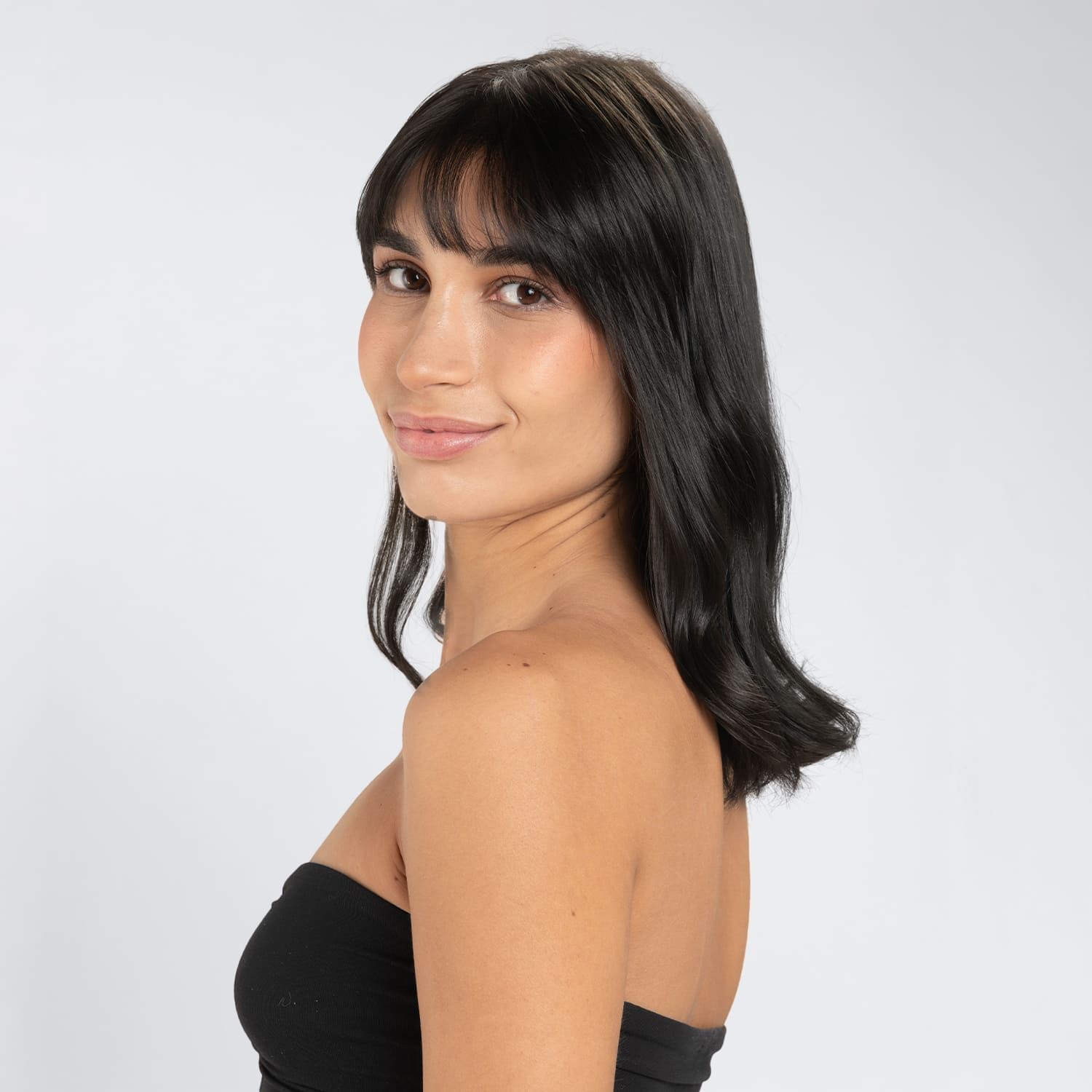 Mulher com cabelo liso e castanho escuro brilhante após aplicar a coloração Herbatint, sobre fundo claro